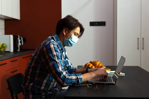 Uomo in maschera sterile digitando sul computer portatile a casa — Foto Stock