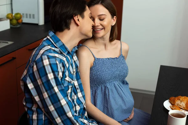 Fröhliche zukünftige Eltern kuscheln beim Frühstück in der Küche — Stockfoto