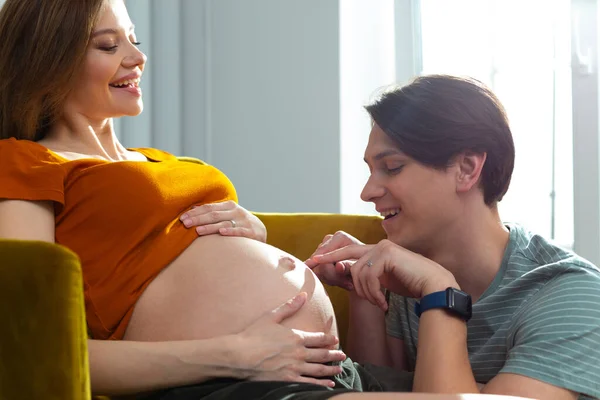 Positiver Mann zeigt auf den Bauchnabel seiner schwangeren Frau — Stockfoto