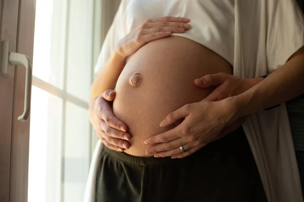 Gravid kvinna och två par händer på magen — Stockfoto