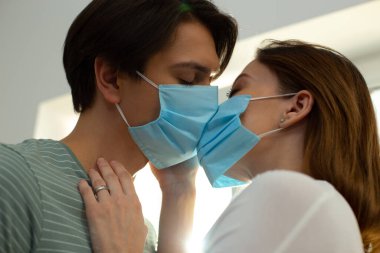 Yüzlerinde tıbbi maskelerle öpüşen bir adam ve kadın.