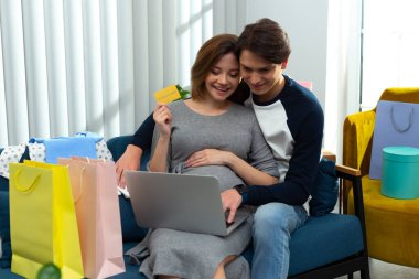 Kocasıyla internetten alışveriş yapan neşeli hamile kadın.