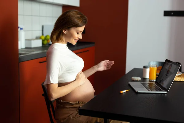 Щаслива вагітна леді дивиться на її живіт під час розмови з лікарем — стокове фото