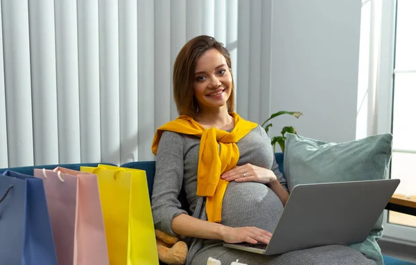 Senhora grávida agradável com presentes e laptop moderno — Fotografia de Stock