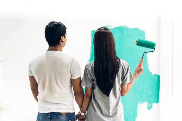 Feliz pareja usando un rodillo de pintura y paredes de pintura en su ne — Foto de Stock