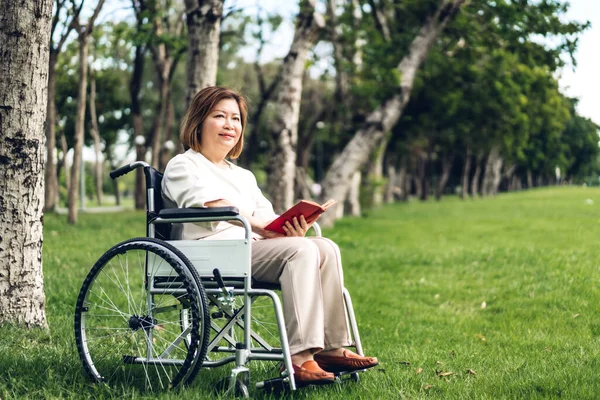 Kıdemli yetişkin yaşlı asya kadınlar tekerlekli sandalye ve okuma bo oturup — Stok fotoğraf