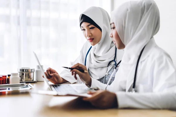 Дві мусульманські азіатські жінки-лікар, що працюють з буфером і ноутбуком — стокове фото
