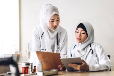 İki Müslüman Asyalı kadın doktor dosya ve dizüstü bilgisayarla çalışıyor.
