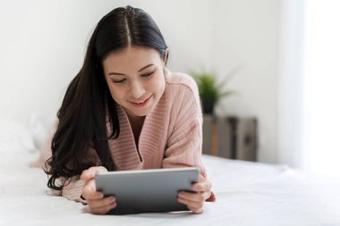 Mutlu kadın evde yatakta tablet bilgisayar kullanarak rahatlatıcı.te