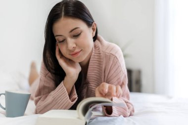 Genç kadın rahatlatıcı ve evde yatakta kitap okuma
