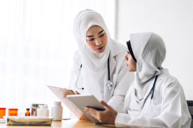 İki Müslüman Asyalı kadın doktor. Pano ve tabletle çalışıyorlar.