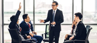 Danışma toplantısı konferans seminerinde bir grup insanın önünde duran ve salon veya seminer odasında soruları cevaplamak için elini gösteren bir işadamı. Sunum ve koçluk kavramı