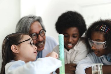 Bir grup genç öğrenci kimyasal bir deney yapıyor ve deney tüpünü okuldaki laboratuvar sınıfında ellerinde tutuyorlar. Eğitim konsepti.