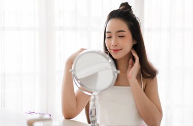 Gülümseyen genç güzel kadın taze sağlıklı cilt evde ayarlanmış makyaj kozmetik ile aynaya bakıyor.yüz güzelliği ve kozmetik konsepti