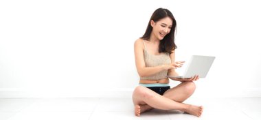 Güzel Asyalı kadın dijital dizüstü bilgisayar kullanıyor sosyal uygulamaları kontrol ediyor ve beyaz duvar arkaplanlı metin eklemek için yerde oturup fotokopi uzayı ile karşılaştırıyor. Kablosuz teknoloji kavramı