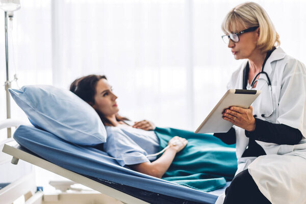 Doctor discussing and consulting check up information on tablet computer with female patien on the bed in hospital.healthcare and medicine