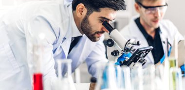 Profesyonel bilim adamı mikroskopla araştırma ve çalışma yapıyor. Genç bilim adamı biyomedikal laboratuvarda kimyasalları analiz ederken ve karıştırırken kimyasal bir deney yapıyor.