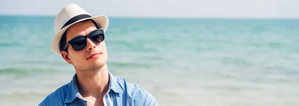 幸せなハンサムな男のモデルの笑顔の肖像は 熱帯のビーチに立っているファッショナブルなサングラスやヒップスター夏のわらの帽子で楽しんでリラックスしてカメラを見てください — ストック写真