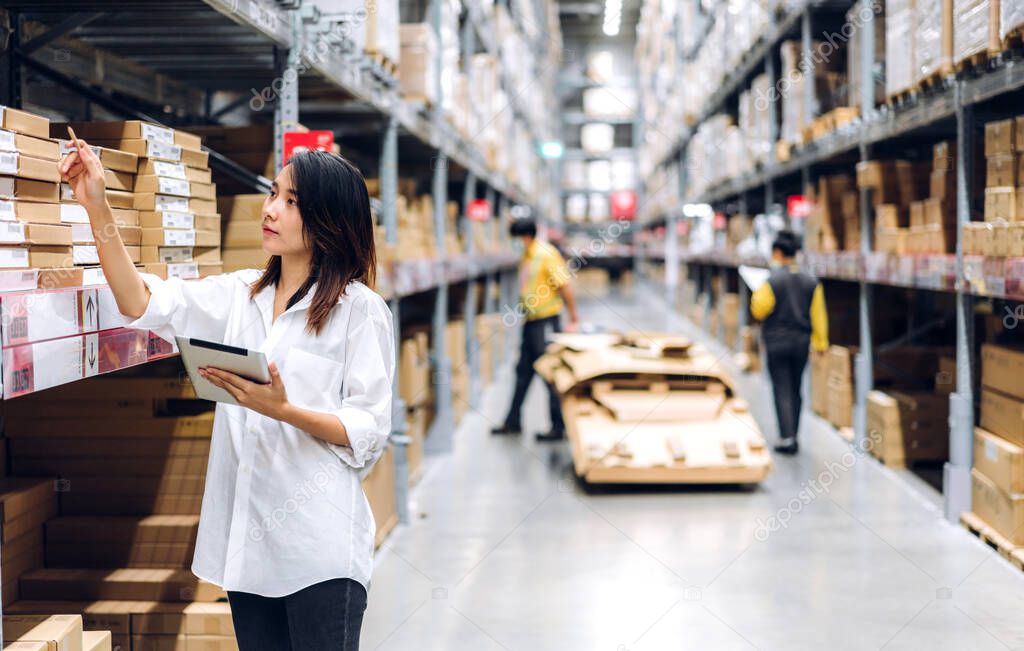 Portrait of smiling asian manager worker woman standing and order details on tablet computer for checking goods and supplies on shelves with goods background in warehouse.logistic and business export