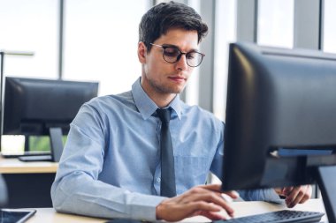 Masaüstü bilgisayar monitörü teknolojisine bakarak rahatlayan yakışıklı iş adamı. Ofiste çalışan ve klavyede yazan genç yaratıcı iş arkadaşları.