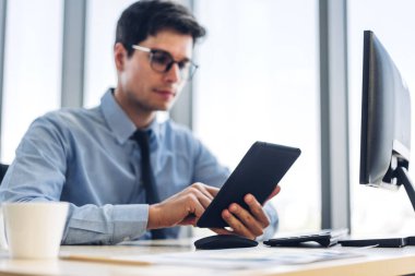 Sandalyeye otururken tablet bilgisayar teknolojisine bakan yakışıklı, kendine güvenen iş adamı. İş günlerinde iş arkadaşları yöneticileri iş yerinde bir fincan kahveyle birlikte iş adamları.