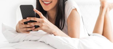 Gülümseyen mutlu Asyalı kadın portresi dijital akıllı telefon kullanarak rahatlıyor. Genç Asyalı kız ekranda yazı yazma ve evde oyun oynama veya sosyal medya oyunlarına bakıyor.