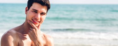 Gülümseyen yakışıklı seksi adamın portresi kaslı vücudunu gösteriyor tropik plajda durup eğleniyor ve Camara 'ya bakıyor.