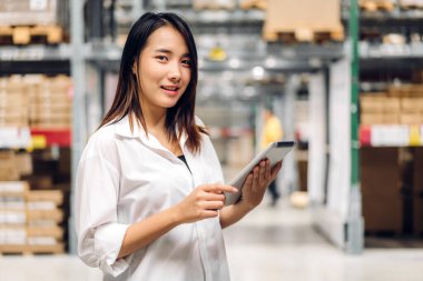 Deponun arka planında bulunan raflardaki kameralara bakan malzeme için tablet bilgisayardan kadın yöneticisinin portresi. Lojistik ve iş ihracatı