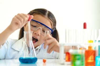 Şirin küçük kız öğrenci araştırma yapmayı ve kimyasal deney yapmayı öğrenirken fen bilimleri sınıfında sıvıyı analiz edip karıştırıyor. Eğitim ve bilim konsepti.