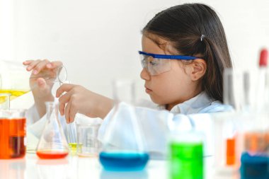 Şirin küçük kız öğrenci araştırma yapmayı ve kimyasal deney yapmayı öğrenirken fen bilimleri sınıfında sıvıyı analiz edip karıştırıyor. Eğitim ve bilim konsepti.
