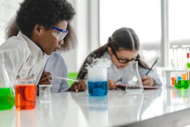 Okuldaki deney laboratuarında test tüpünde sıvı karıştırırken ve analiz ederken araştırma yapmayı öğrenen ve kimyasal deney yapan bir grup küçük sevimli öğrenci. Eğitim.