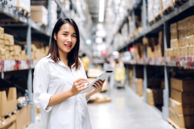 Deponun arka planında bulunan raflardaki kameralara bakan malzeme için tablet bilgisayardan kadın yöneticisinin portresi. Lojistik ve iş ihracatı