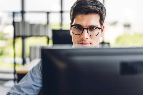 Masaüstü bilgisayar monitörü teknolojisine bakarak rahatlayan yakışıklı iş adamı. Ofiste çalışan ve klavyede yazan genç yaratıcı iş arkadaşları.