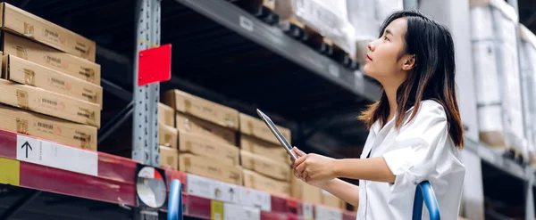 Portrait of smiling asian manager worker woman standing and order details on tablet computer for checking goods and supplies on shelves with goods background in warehouse.logistic and business export