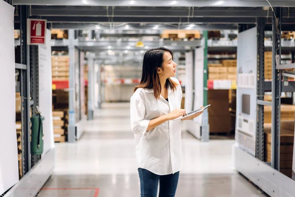 Gülümseyen Asyalı yönetici kadın portresi ayakta duruyor ve malzeme ve gereçleri depoda kontrol etmek için tablet bilgisayardan ayrıntılı talimat veriyor. Lojistik ve iş ihracatı
