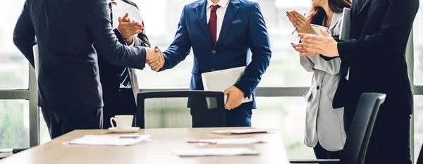 モダンなオフィスでカジュアルなビジネスクラップの手のグループの前で一緒にエレガントなスーツの成功した握手で2つのビジネスパートナーをイメージします — ストック写真