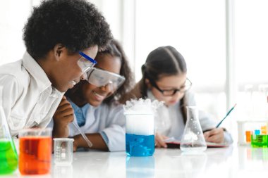 Okuldaki deney laboratuarında test tüpünde sıvı karıştırırken ve analiz ederken araştırma yapmayı öğrenen ve kimyasal deney yapan bir grup küçük sevimli öğrenci. Eğitim.