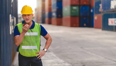 Miğferli profesyonel mühendis konteynır ustabaşı ayakta çalışıyor ve telsiz kullanıyor stokları yükleme için konteynıra koyuyor. Lojistik ve iş ihracatı