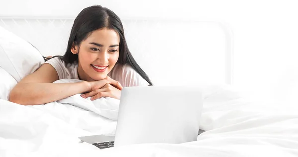 Young asian woman relaxing using laptop computer on bed in the bedroom at home.Young beauty girl working and typing on keyboard at home.work from home concept