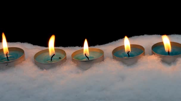 Candles burn in the snow on a black background. — Stock Video