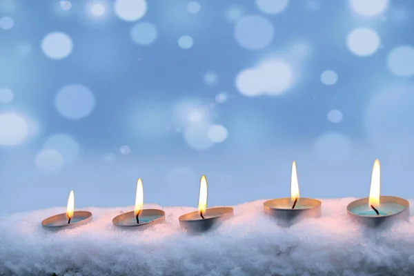 Blue candles burn in the snow on a blue background. — Stock Photo, Image