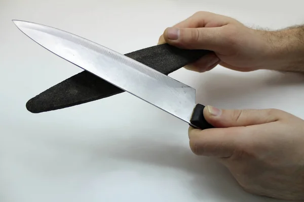 Handen met een slijpsteen en een mes geïsoleerd op een grijze achtergrond — Stockfoto