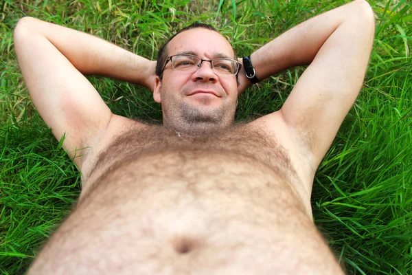 Lusta ember. Egy ember egy nagy hasa fekszik a fűben. — Stock Fotó