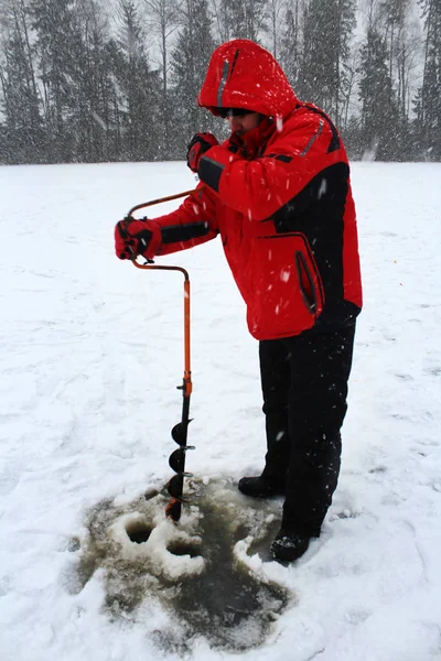 Balık tutma kış. Bir adam buz buz kıracağı ile bir delik matkap.