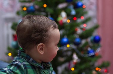 Küçük bir çocuk Noel ağacında duruyor.