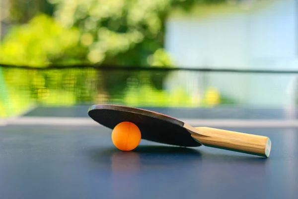 Tafeltennistafel met racket en oranje bal op achtertuin — Stockfoto