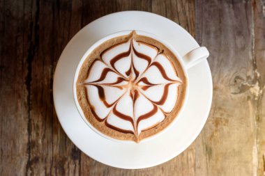 Bir fincan kahve ve ahşap masa üzerinde güzel bir Latte sanatı.