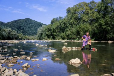 Kız bir dağ manzarası poz. Güzel dağ manzarası. Kız mor bir elbise giymiş. Genç bir kız suda diz boyu duruyor. Göz alıcı bir kız doğada dinleniyor. Bir hippi kız.