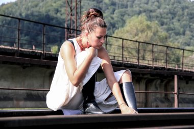 Güzel esmer siyah çizmeler ve beyaz bir elbise. Bir kadın için tren bekliyor. Bir kadın doğada dinleniyor. Arka plan demiryolu.