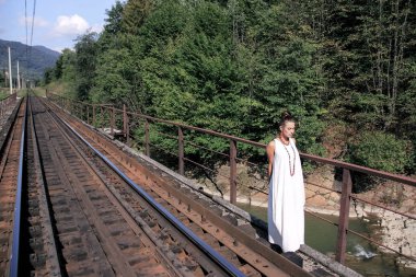 Pamuk Beyaz giysili bir kadına. Arka plan demiryolu kız. Kız için tren bekliyor. Cutie fotoğrafçısına poz veriyor. Çekici kadın dağ manzarası Gürcistan'ın arka planda. Utangaç kız. Dağlar, Gürcistan.